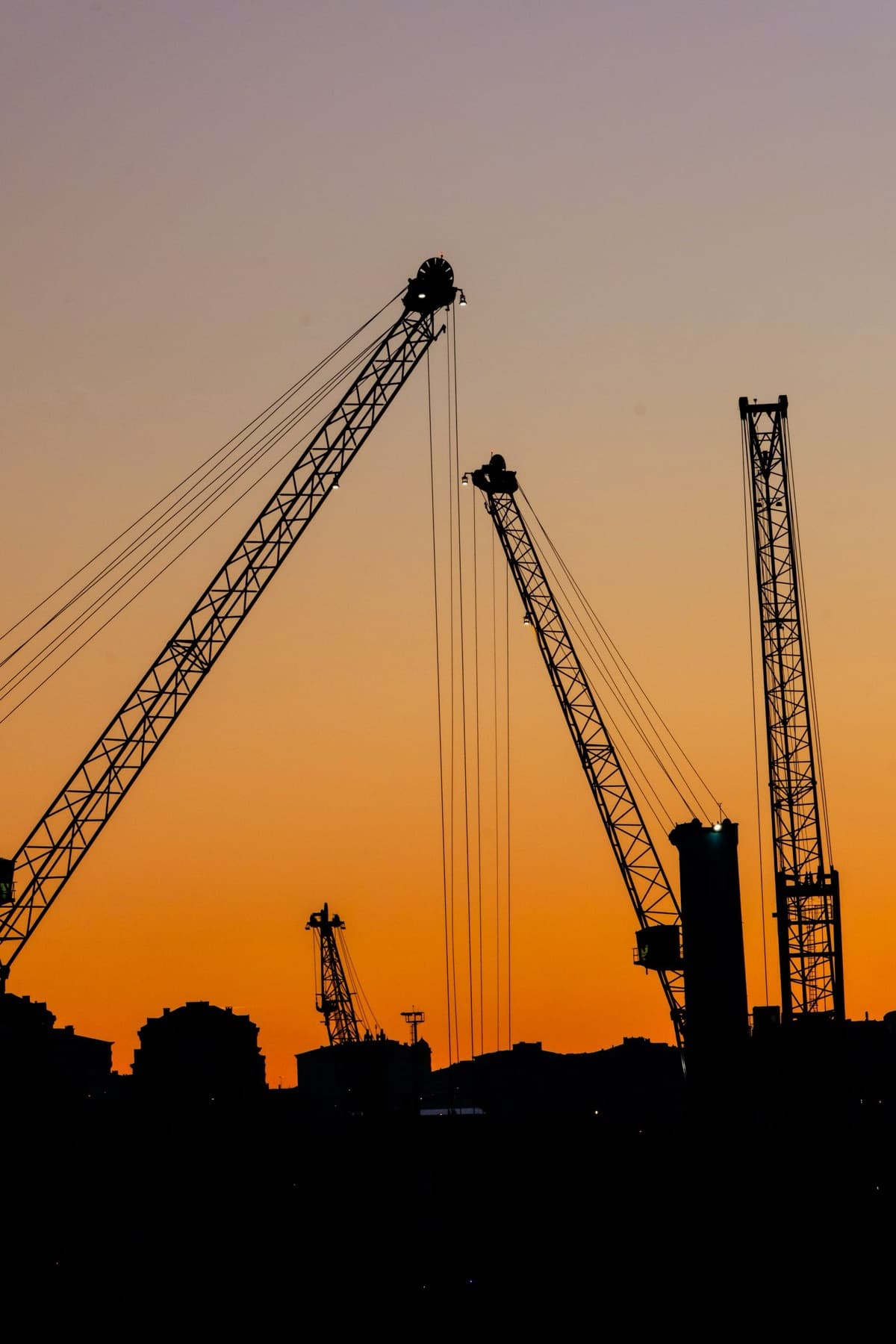 Tower cranes over a construction site at dusk. The kind of real, asset-heavy, cash-flowing business the machine acquires.